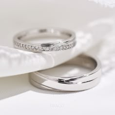 two wedding rings sitting on top of each other next to a white cloth covered pillow