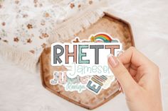 a person holding up a sticker that says rhettt jamesen on it