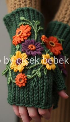 a woman's hand holding a green knitted mitt with flowers on it