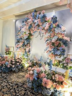 an elaborate floral display with blue and pink flowers on the wall, surrounded by gold chairs