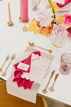 the table is set with pink and yellow flowers, silverware, and napkins