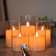 a person is holding a remote control in front of candles with one hand on the table