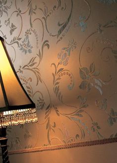 a lamp on a table next to a wallpapered wall with an intricate design