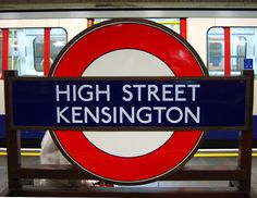 a sign that says high street kensington on the side of a train platform