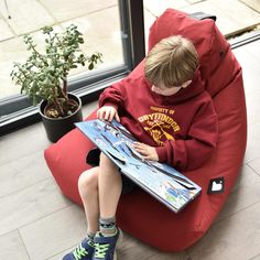 a young boy sitting on a bean bag chair looking at a map and potted plant