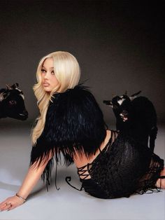 a woman in black dress laying on the ground next to two cows with long blonde hair