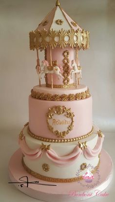 a pink and white cake with gold trimmings on the top is decorated with a carousel