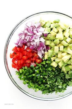 chopped vegetables are in a bowl on a white surface, including red onion, green onions and avocado