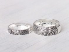 two fingerprint wedding rings with names engraved on the sides, one in white gold or silver