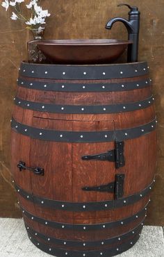 a large wooden barrel with metal straps and rivets on the bottom, in front of a brown wall