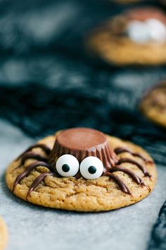 a cookie with googly eyes and a chocolate spider on it's face is sitting in front of other cookies