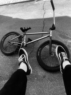 a person standing next to a bike on the street with their feet propped up against it