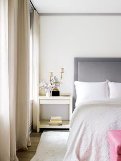 a bed with white sheets and pillows next to a pink bench in front of a window