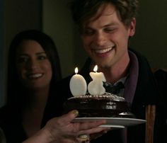 a man holding a plate with a cake on it and two lit candles sticking out of it