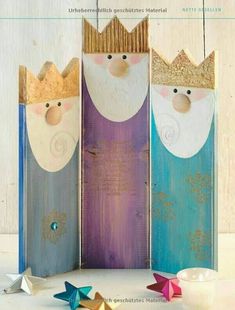 three wooden dolls with crowns on them sitting in front of a white wall and two small stars