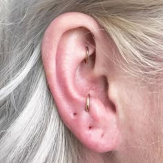 a close up of a person with blonde hair wearing two gold ear piercings on their ears