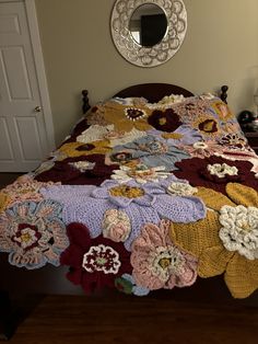 a bed covered in a blanket with crocheted flowers on it and a mirror above