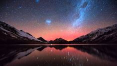 the night sky is filled with stars above mountains and water, as seen from a lake