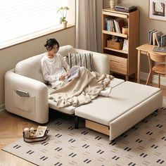 a woman sitting on top of a white couch under a blanket in a living room