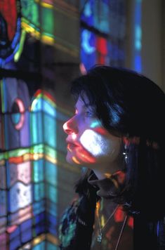 a woman standing in front of a stained glass window with the light coming through it