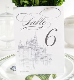 there is a place card on top of a plate with flowers in the middle and a castle behind it