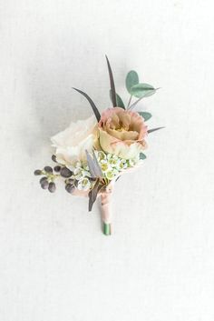 a boutonniere with flowers and greenery on the side against a white wall