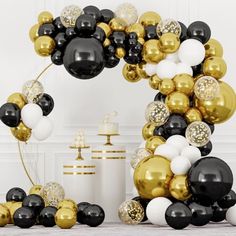 a black and gold balloon arch with white and gold balloons on the top, along with other decorations