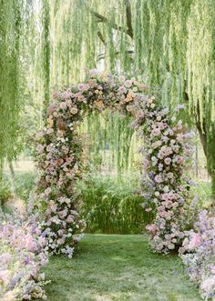 an outdoor wedding ceremony with pink flowers and greenery on the grass, surrounded by willow trees