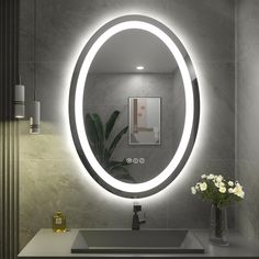 a bathroom sink with a round mirror above it and flowers in the vase on the counter