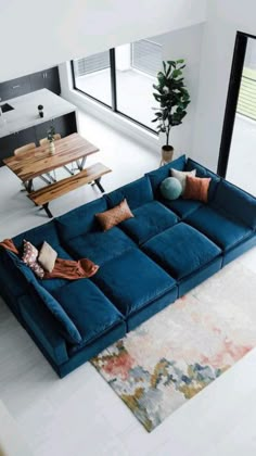 a large blue couch sitting in a living room next to a wooden table and windows