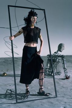 a woman standing in front of a mirror on top of a desert ground with an object behind her