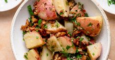 a white bowl filled with potatoes and meat on top of a wooden table next to other plates