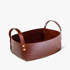 a brown leather basket with two handles on the front and one handle at the bottom