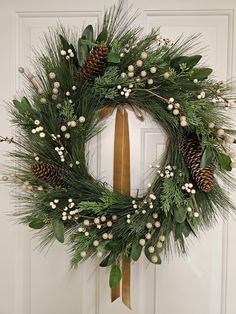 a wreath with pine cones and berries hanging on a door