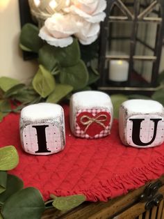 three small blocks with the letter u on them sitting on a red blanket next to flowers