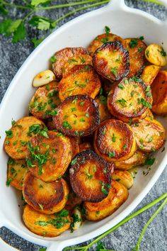 a white casserole dish filled with potatoes and parsley garnished with herbs