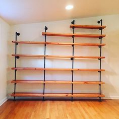 an empty room with wooden shelves and black pipe shelving units on the wall,