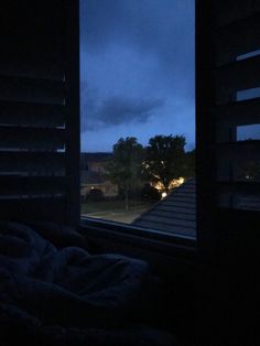 an open window in a dark room with the night sky seen through it and trees outside