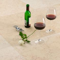 two wine glasses and a bottle of wine on a marble table top with white flowers