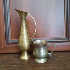 two metal pitchers sitting next to each other on a wooden table in front of a door