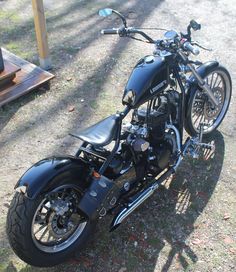 a black motorcycle parked on top of a grass covered field next to a wooden structure