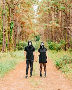 two people with painted faces holding hands on a dirt path in the woods, wearing black