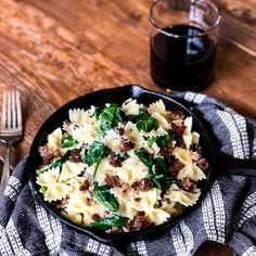 a skillet filled with pasta and spinach on top of a table next to a glass of wine