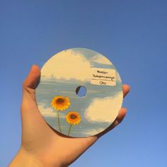 a person holding up a painted disc with flowers on it in front of a blue sky