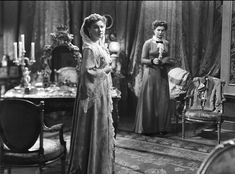 an old black and white photo of two women standing in front of a dining room table