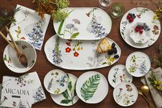 the table is covered with plates and place settings for various foods, flowers, and herbs