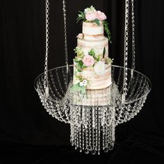 a three tiered wedding cake with flowers and chains hanging from the side on a glass platter