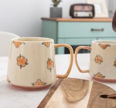 two coffee mugs sitting on top of a white table next to a cutting board