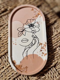 a pink and white tray with a flower on it sitting on a wicker surface