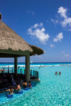 people are swimming in the blue water at an ocean resort with thatched roof huts